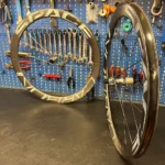 Due ruote WS ROAD Revolution CarbonSpokes Hookless - 1162gr appoggiate su un tavolo da lavoro e parete tappezzata da attrezzi per biciclette